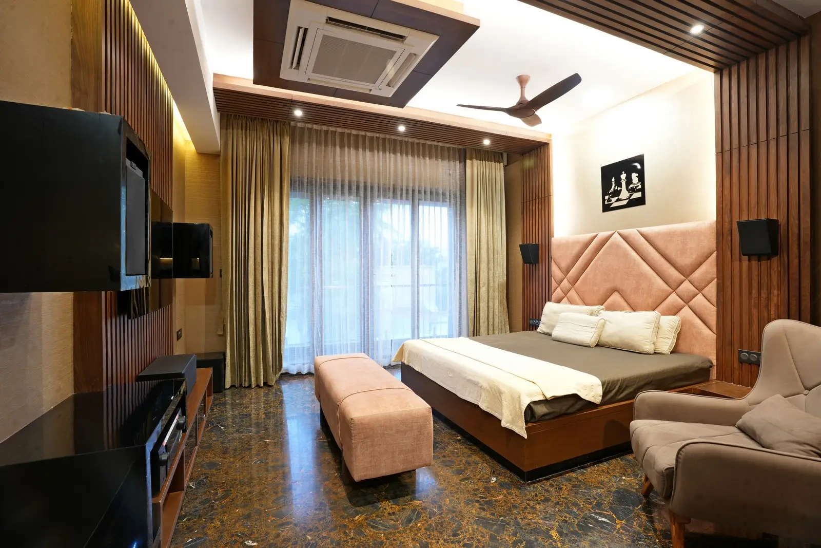 An elegant bedroom featuring a tufted headboard, marble flooring, warm wooden paneling, soft lighting, and large glass doors with sheer curtains.