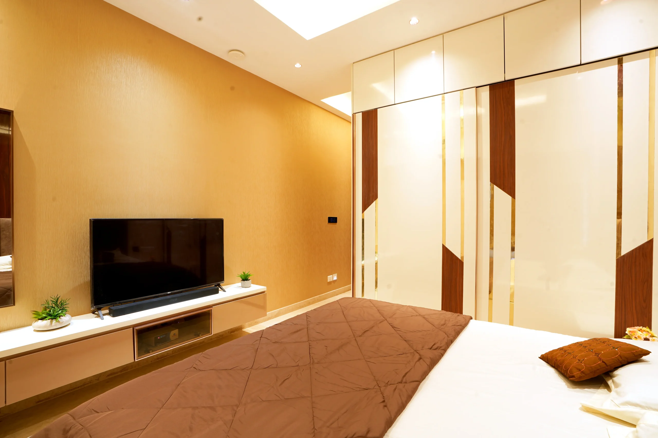 Functional elements like the cushioned window seating, sleek floating TV unit, and geometric wardrobe design add practicality while enhancing the room’s contemporary sophistication.