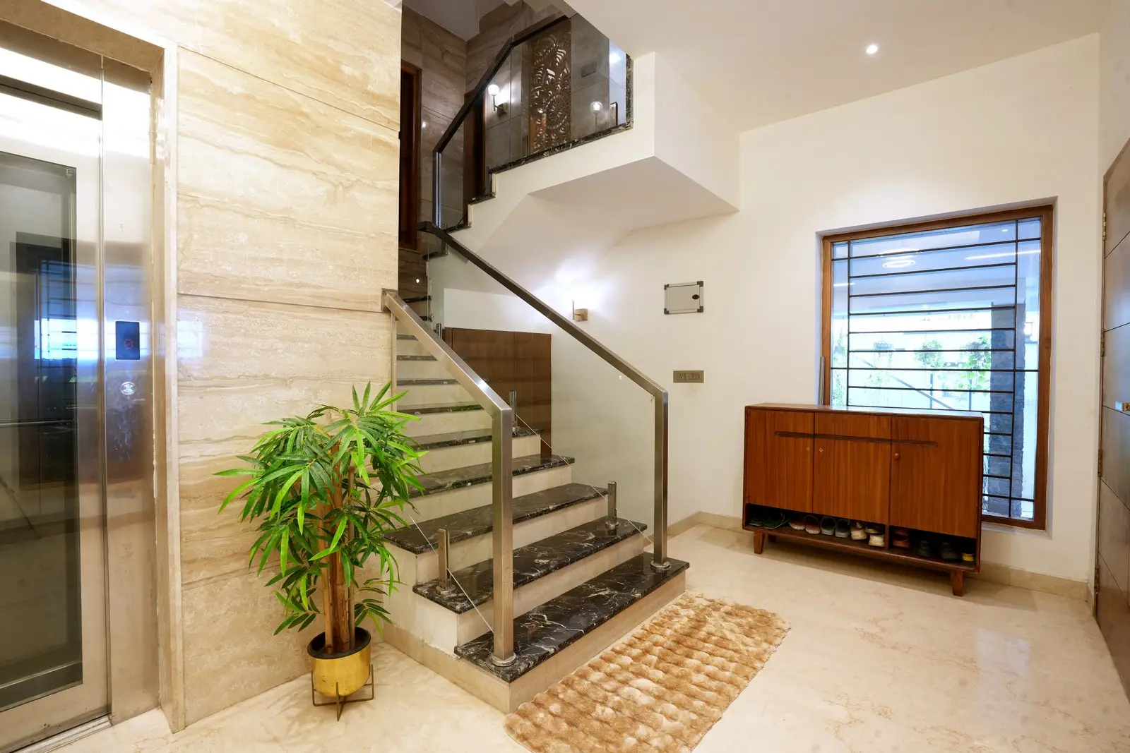 A sophisticated interior staircase with glossy marble steps, glass railings, soft wall lighting, and tasteful greenery enhancing the modern ambiance.

