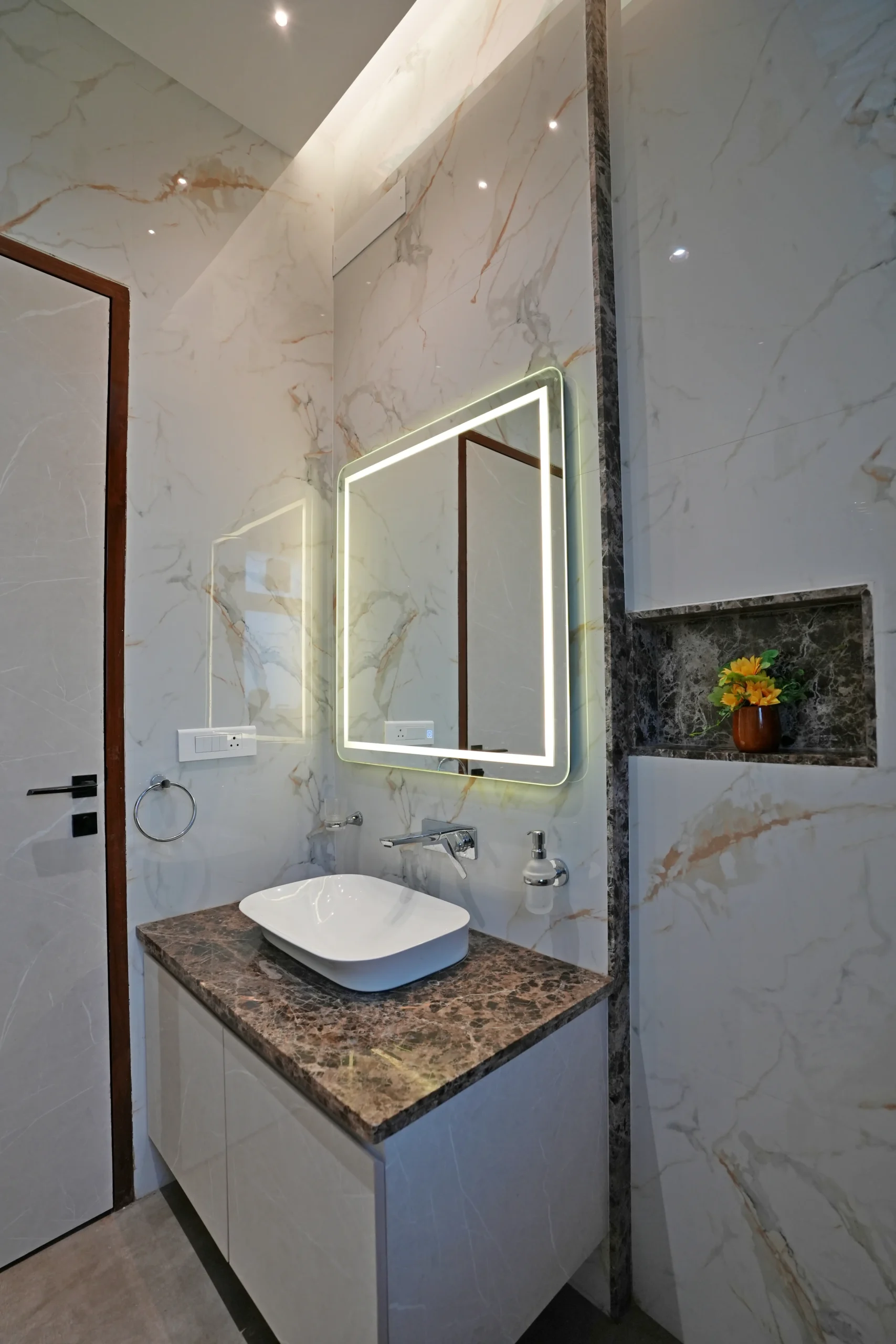 This bathroom showcases a modern, elegant design with marble-effect walls, a dark brown countertop, a vessel sink, and an illuminated LED mirror.