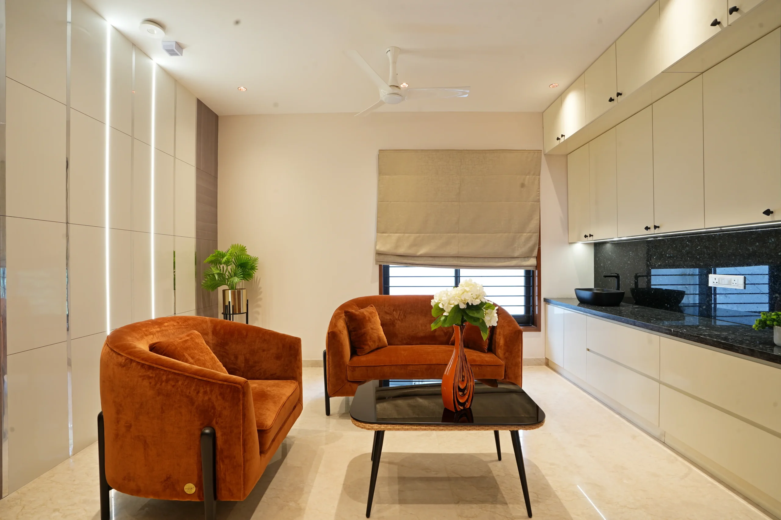 Second Floor -this modern living space features rust-orange velvet armchairs, a sleek black coffee table, beige cabinetry, and marble flooring, creating a warm, elegant ambiance.