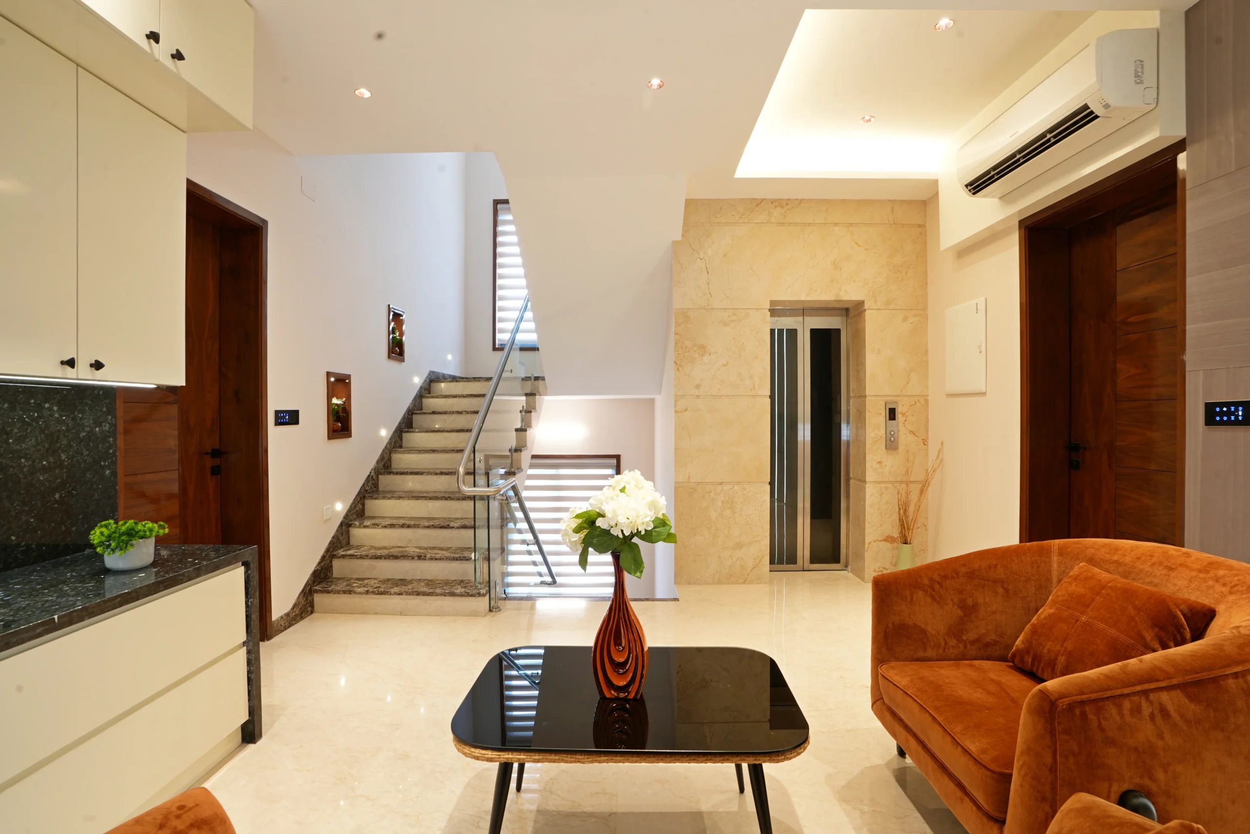 The elegantly designed interior highlights a harmonious blend of warm tones and premium finishes, featuring marble flooring, rust-orange seating, and a glass-paneled elevator.