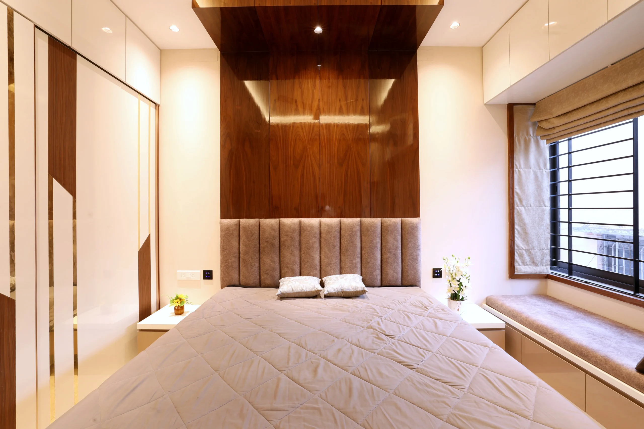 This bedroom features a refined contemporary design with warm neutral tones, a quilted bedspread, a tall upholstered headboard, and a rich wooden accent wall for elegant contrast.