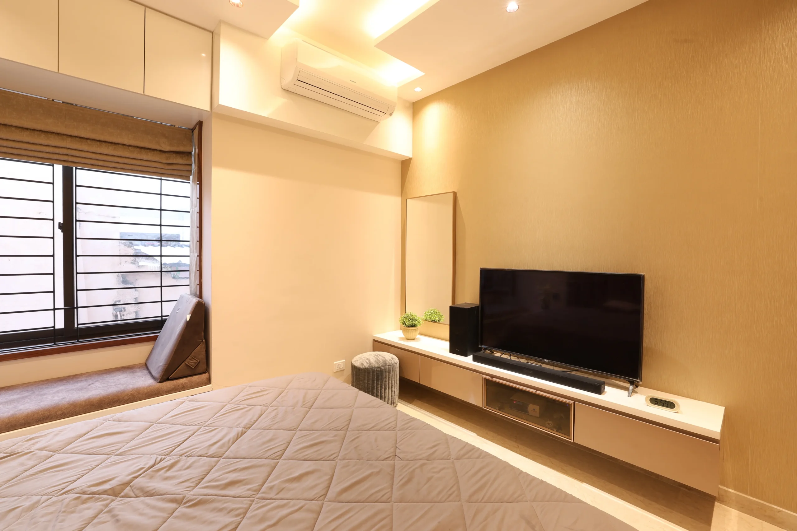 A window with Roman blinds, a cushioned seating nook, overhead cabinets, and integrated air-conditioning complete the serene, cohesive space with comfort, storage, and visual balance.