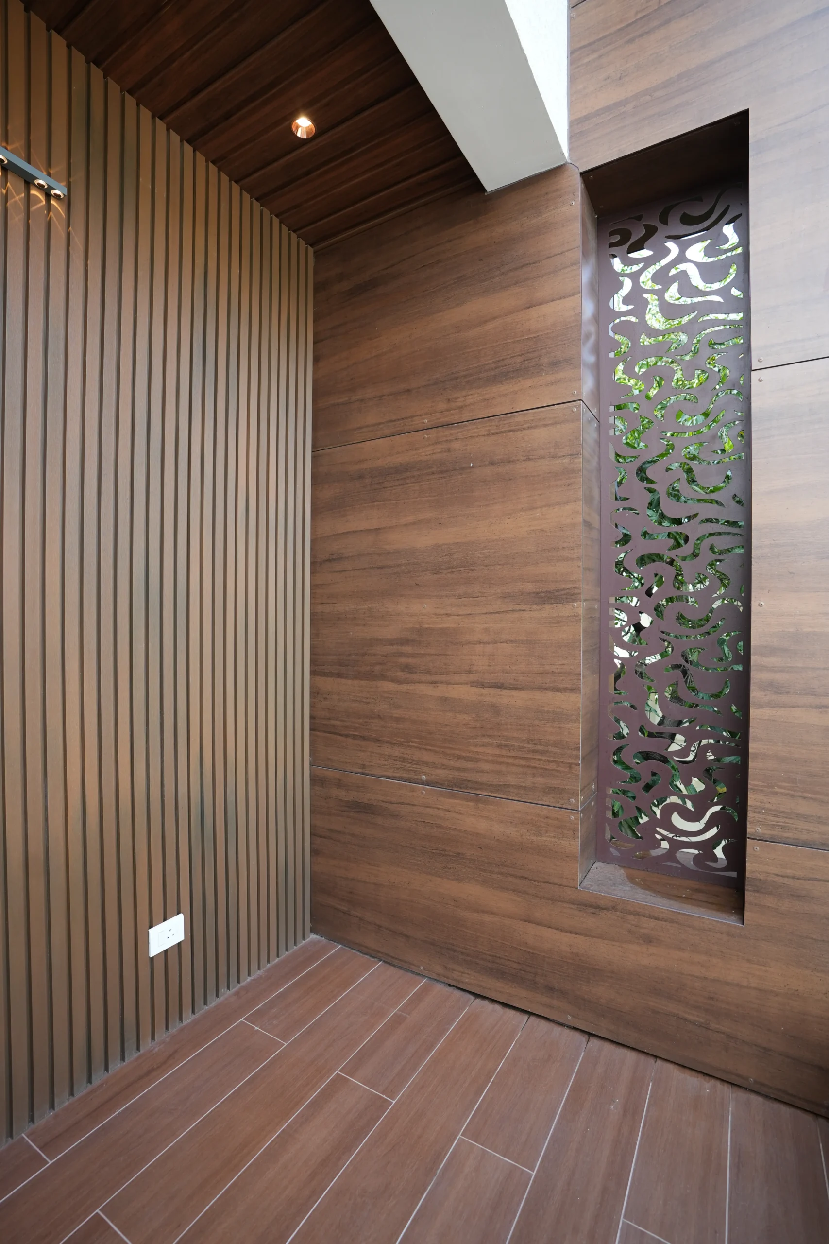 Clear glass railings, stainless steel fittings, laser-cut metal screens, horizontal wooden ceiling panels, and recessed lighting enhance openness, natural light, texture, and modern timeless sophistication.