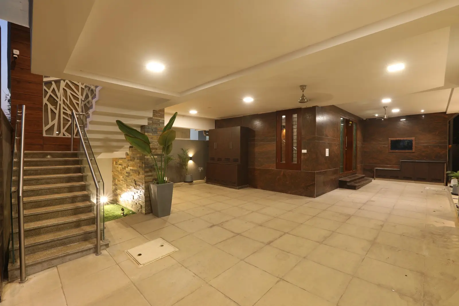 The ground floor - is a spacious parking area with tiled flooring, warm lighting, stone accents, and sleek stairs, offering a refined sense of elegance.

