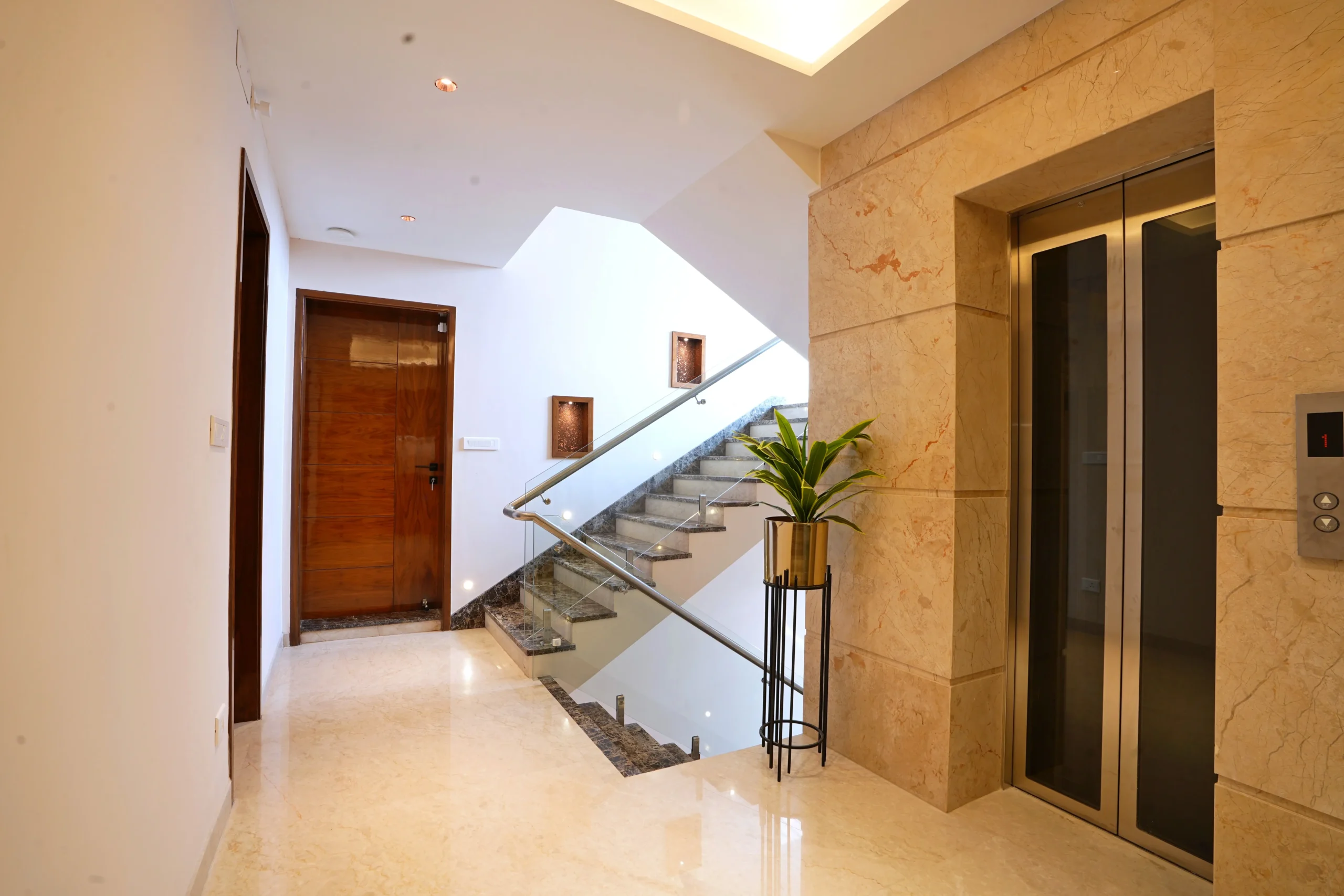 This space features a staircase, elevator, and corridor with polished marble, granite steps, glass railings, stainless-steel accents, recessed lighting, and natural elements for refined elegance.