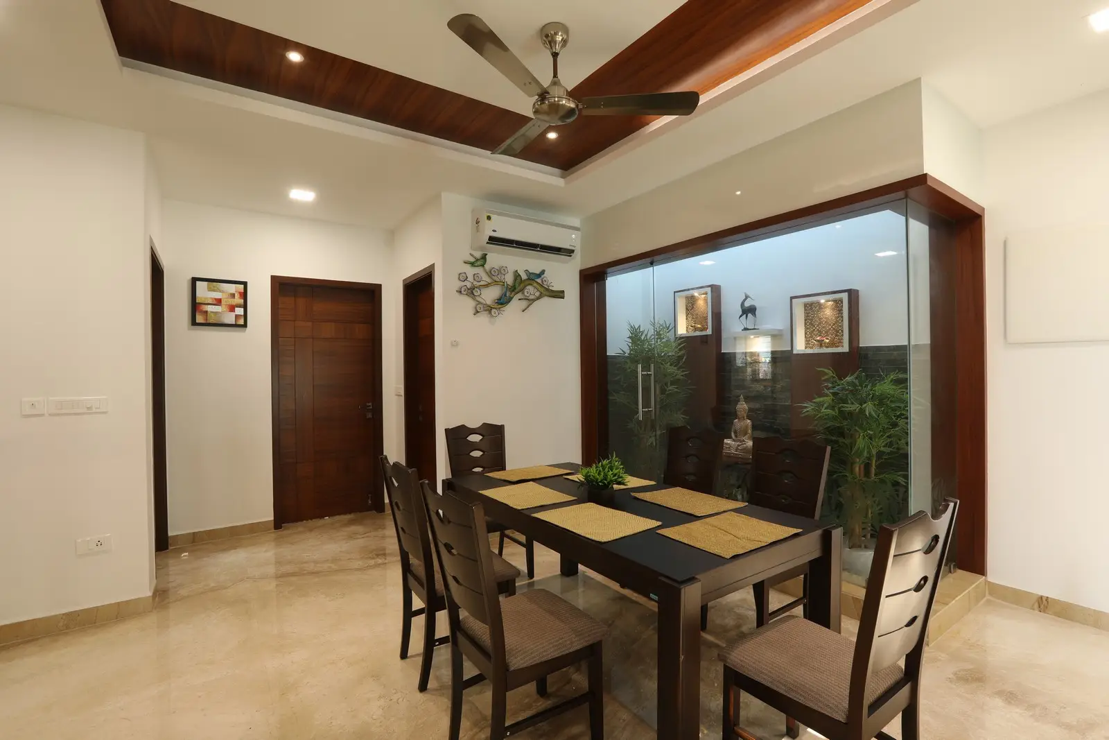 Dining area offers a peaceful atmosphere with warm lighting, wooden accents, and a small courtyard featuring greenery that enhances its natural charm.
