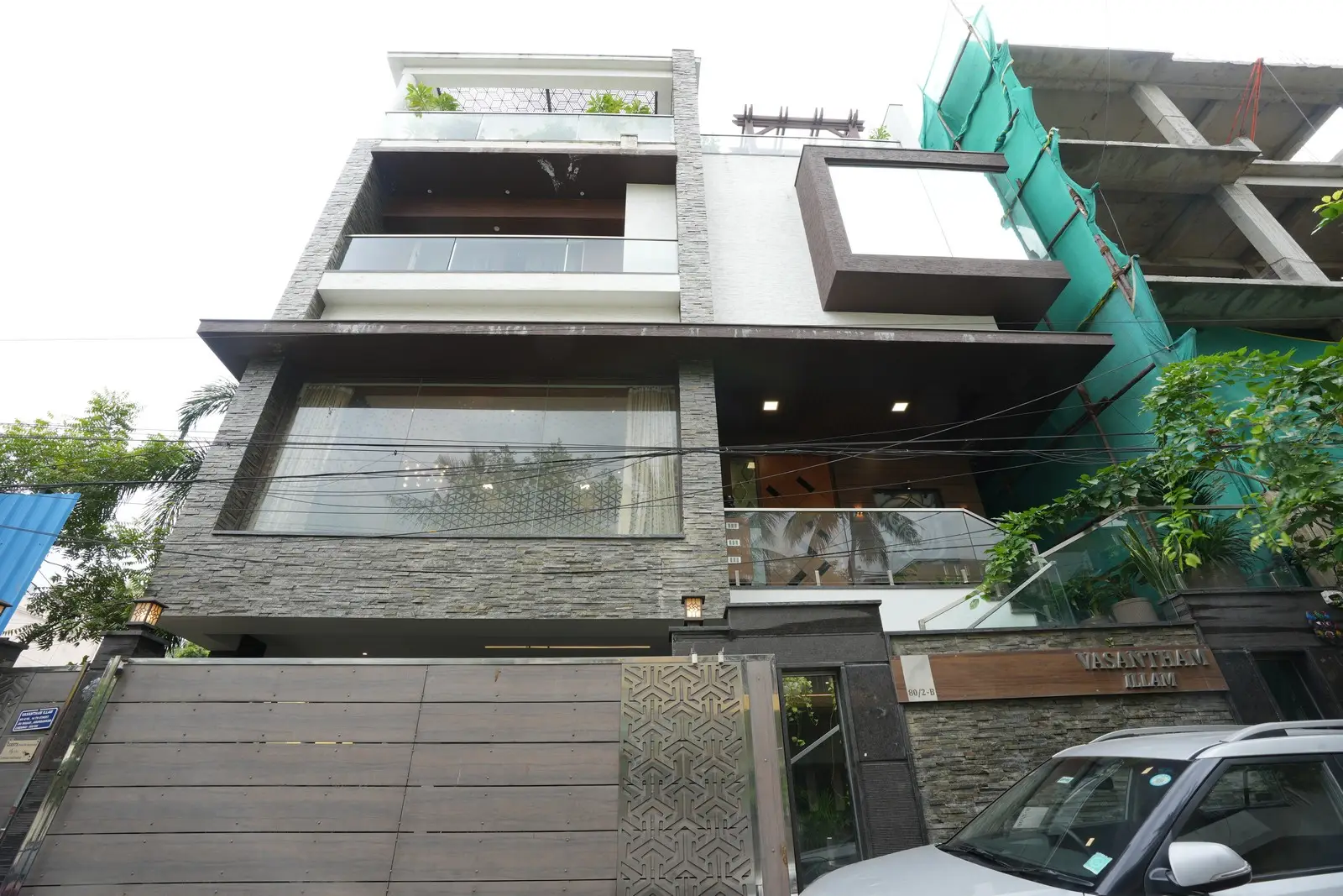 A luxurious multi-story residence with an elegant exterior, featuring stone cladding, glass balconies, wooden accents, and a stylishly designed entrance.

