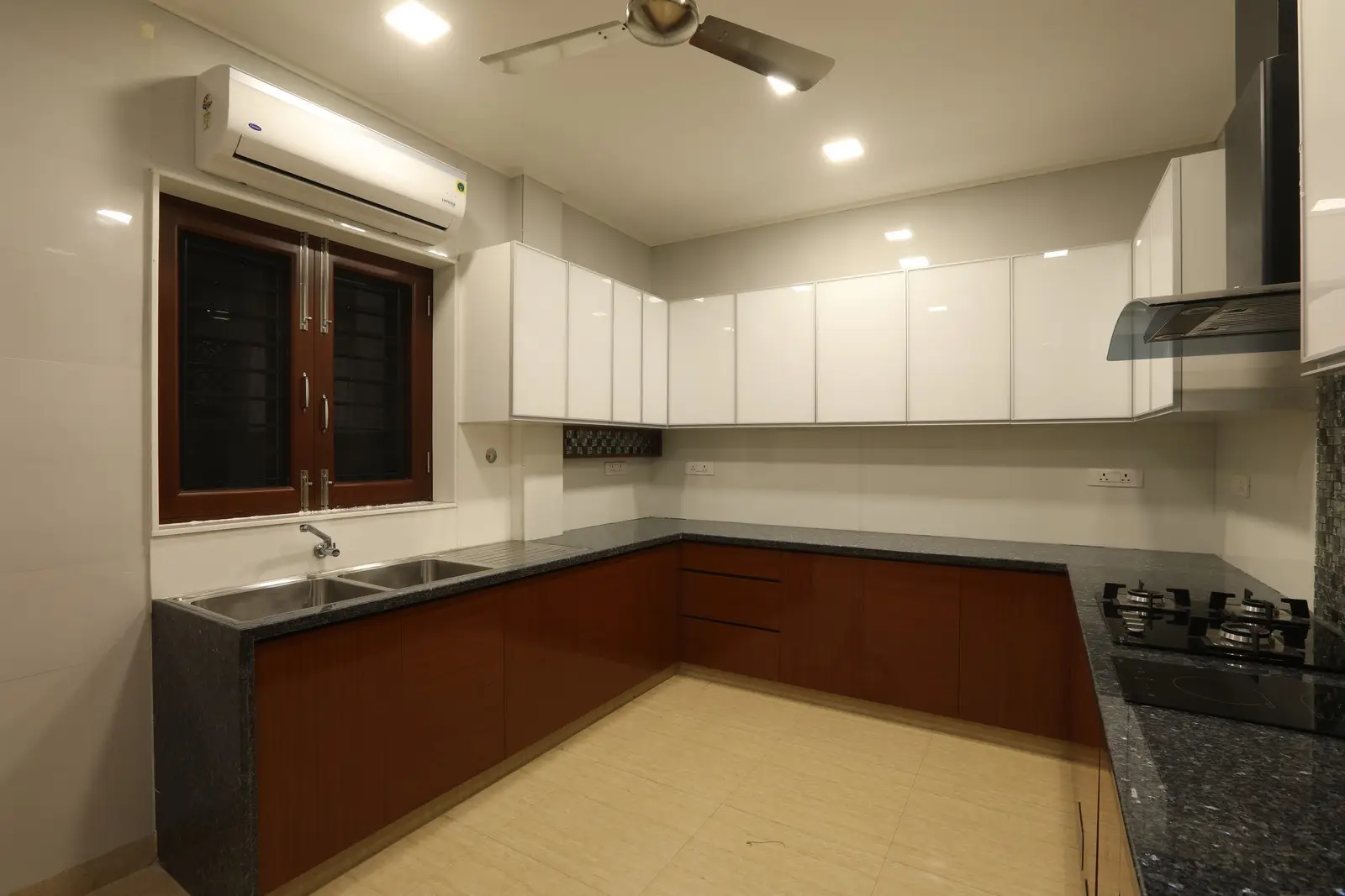 A contemporary L-shaped kitchen featuring glossy white upper cabinets, brown lower cabinets, black granite countertops, recessed lighting, and a ceiling fan for a refined modern look.