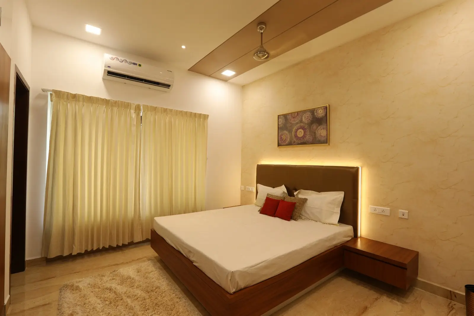 This bedroom features warm lighting, a sleek wooden bed with side tables, soft curtains, and neutral tones, creating a cozy and elegant atmosphere.
