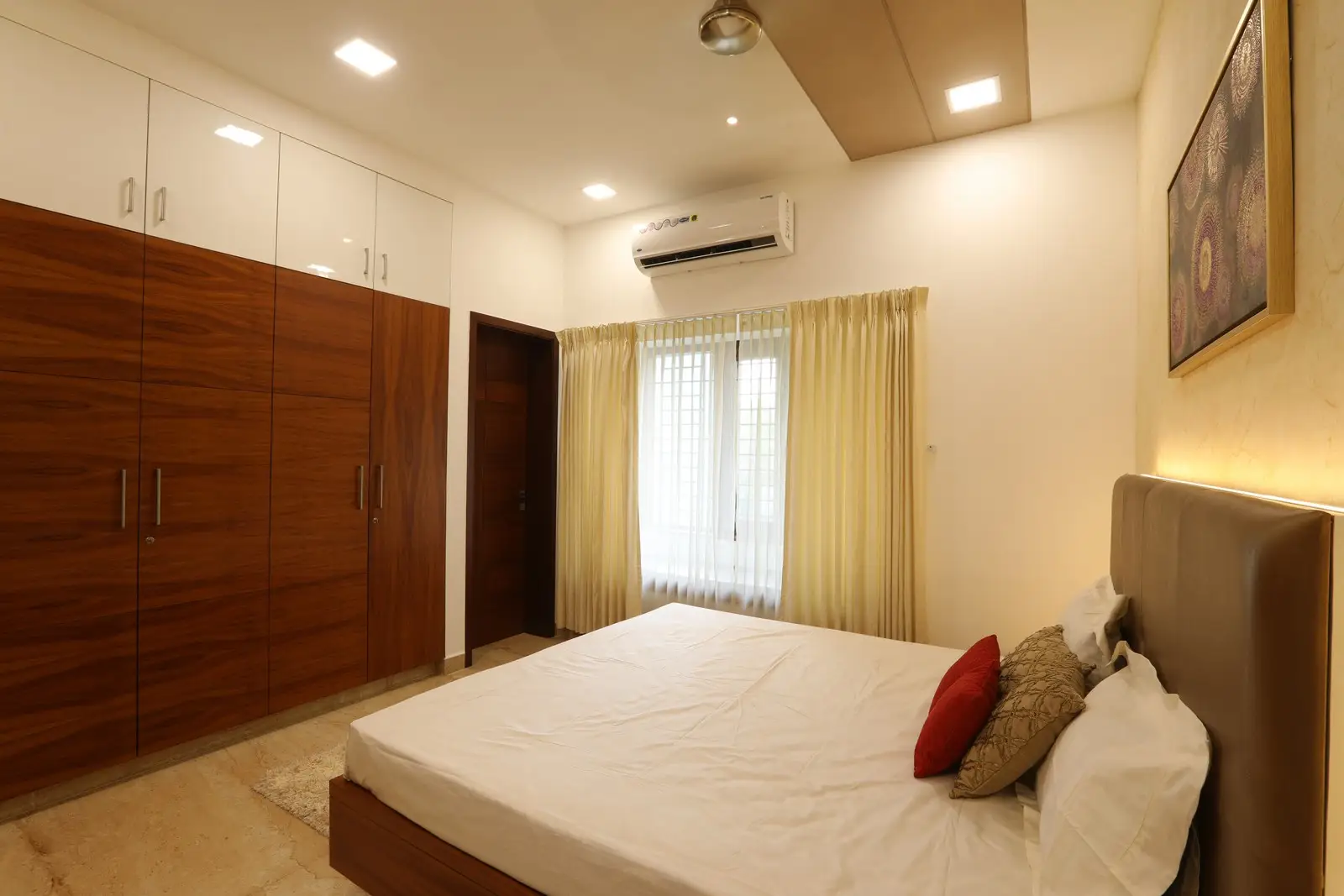 Bedroom presents a bright and airy ambiance with wooden wardrobes, soft beige tones, and natural light enhancing its clean, modern, and comfortable appeal.

