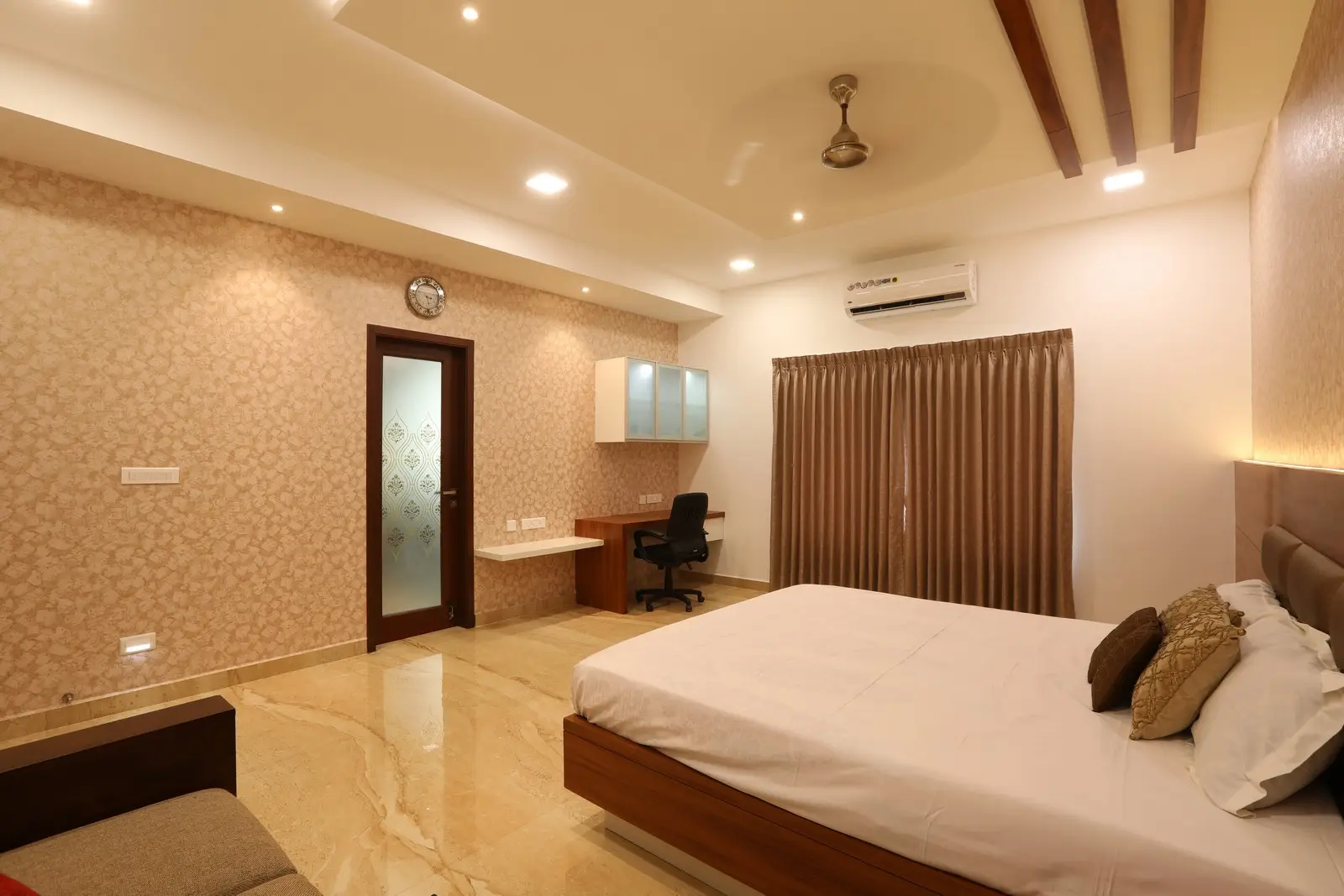 It showcases a refined design with marble flooring, textured wallpaper, a wooden bed frame, ambient lighting, and a compact workspace enhancing modern comfort.
