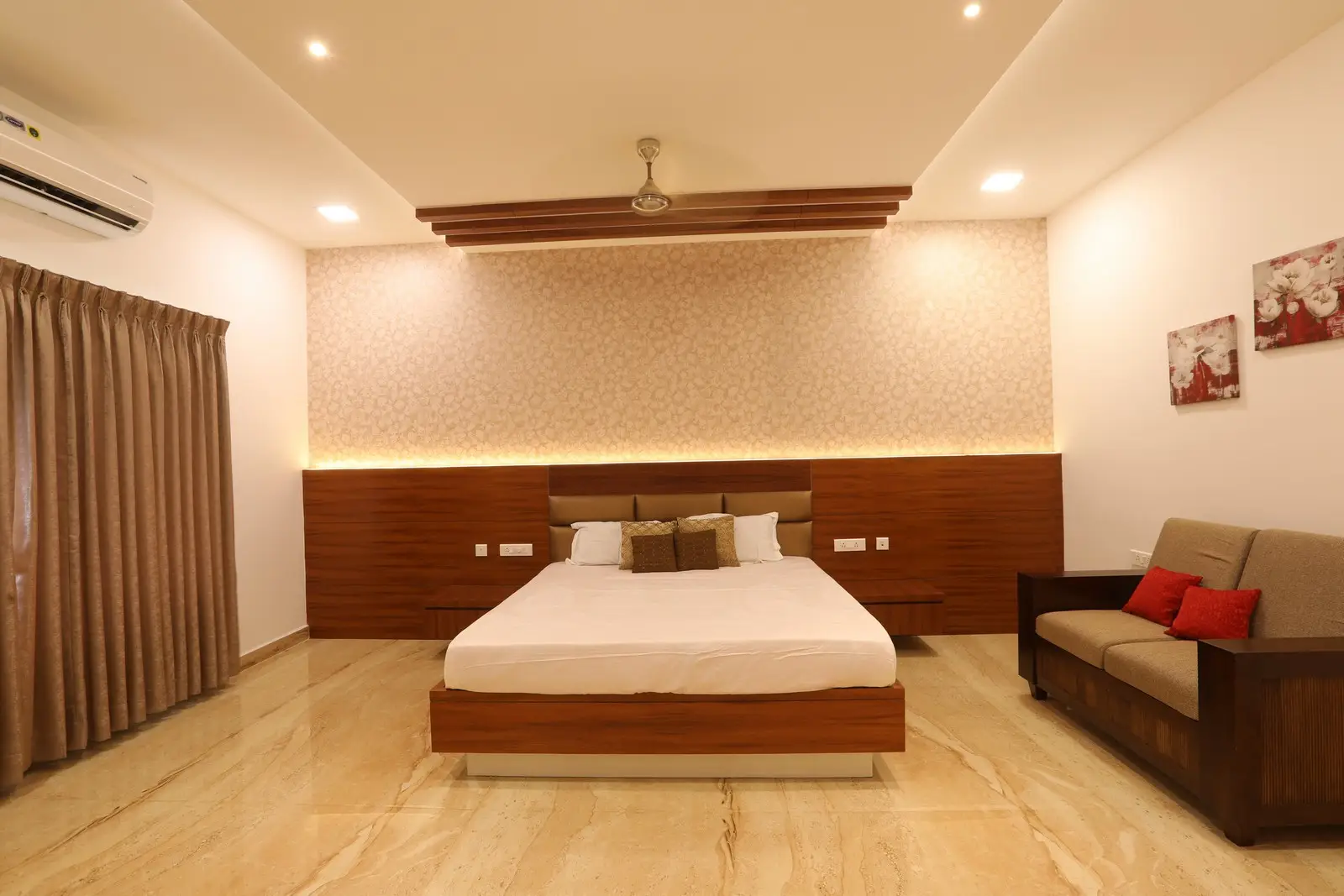 Features a minimalist design with a wooden bed frame, marble flooring, warm recessed lighting, and neutral décor creating a serene, contemporary atmosphere.