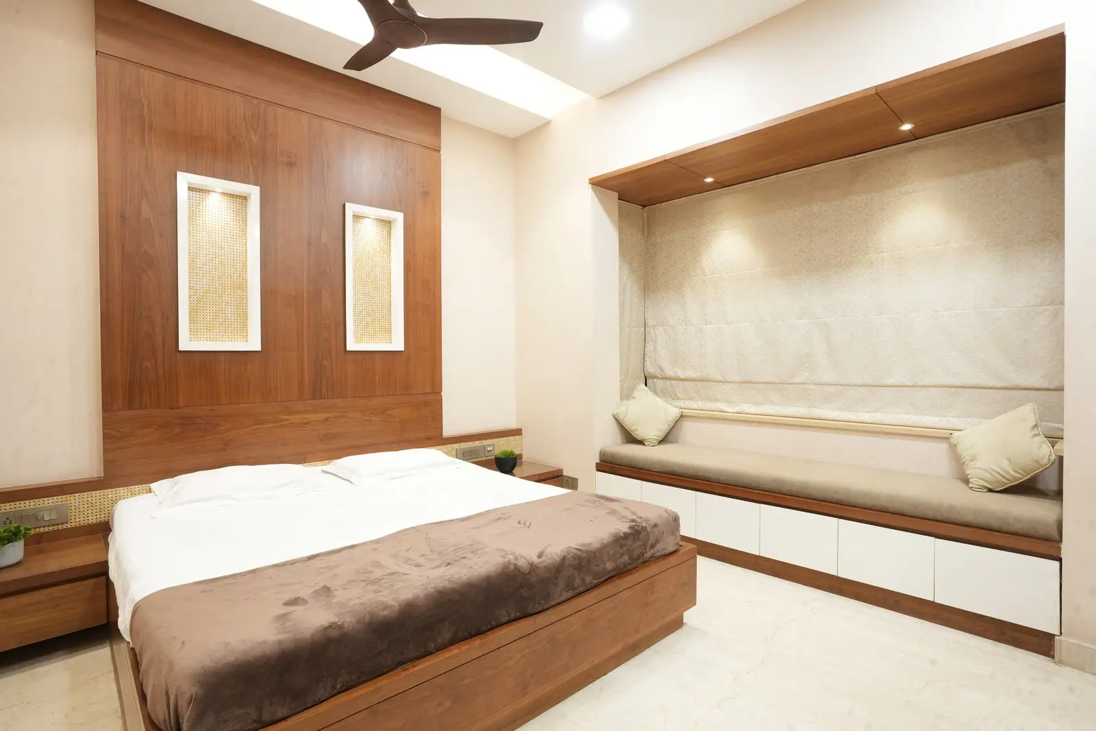 A planned cozy bedroom designed with warm veneers, elegant lighting, thoughtful storage, and a bright U-shaped window seating that enhances comfort and charm.
