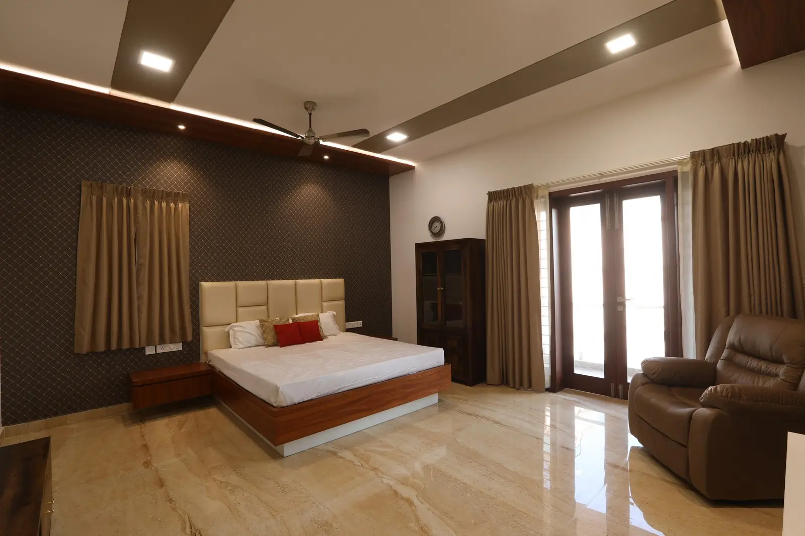 The bedroom presents a luxurious modern design with polished marble flooring, a cushioned headboard bed, warm recessed lighting, and full-length curtains framing elegant glass doors.