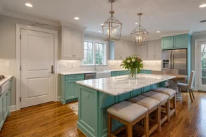 Spacious kitchen with teal lower cabinets and white upper cabinets, featuring a large marble island with cushioned stools, two geometric pendant lights, a stainless steel refrigerator, and a vase of fresh flowers on the island.